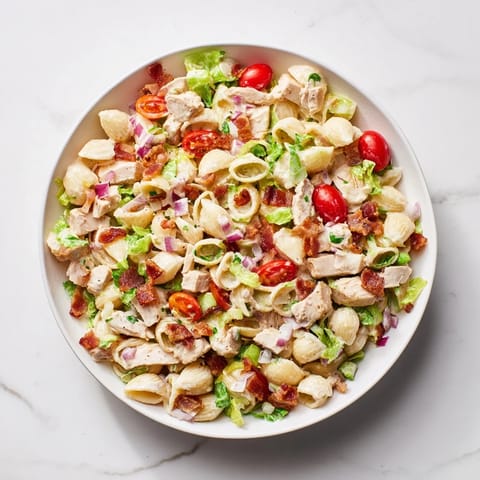 Gelbe und rote Pasta-Schalen mit gekochtem Hühnchen, knusprigem Speck und frischem Gemüse in cremiger Mayo-Dressing auf weißem Teller.  