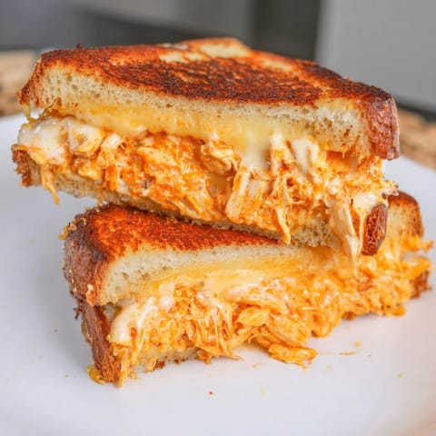 Buffalo Chicken Ranch Grilled Cheese sandwich sliced open, showcasing melted cheddar and shredded buffalo chicken between golden sourdough crusts.  
