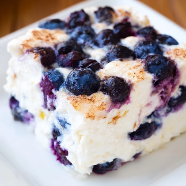 A warm, close-up shot of a baked Blueberry Cottage Cheese Bake, studded with juicy blueberries.